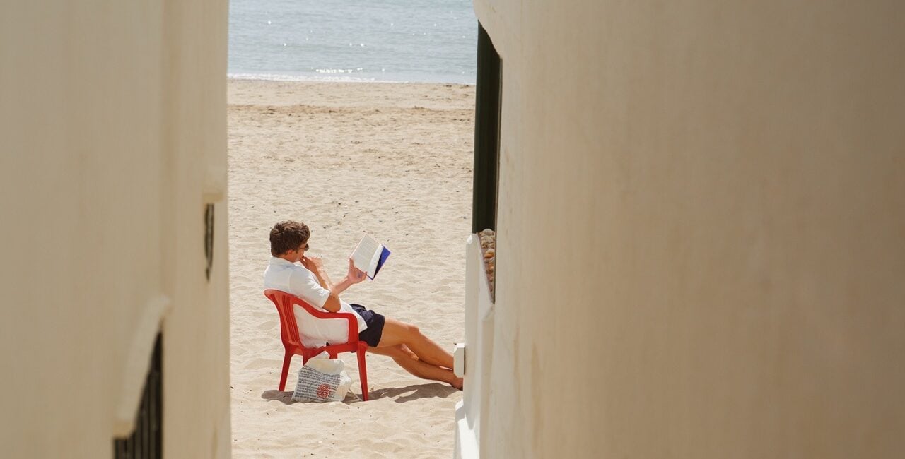 Ein mann sitzt mit einem Buch am Strand