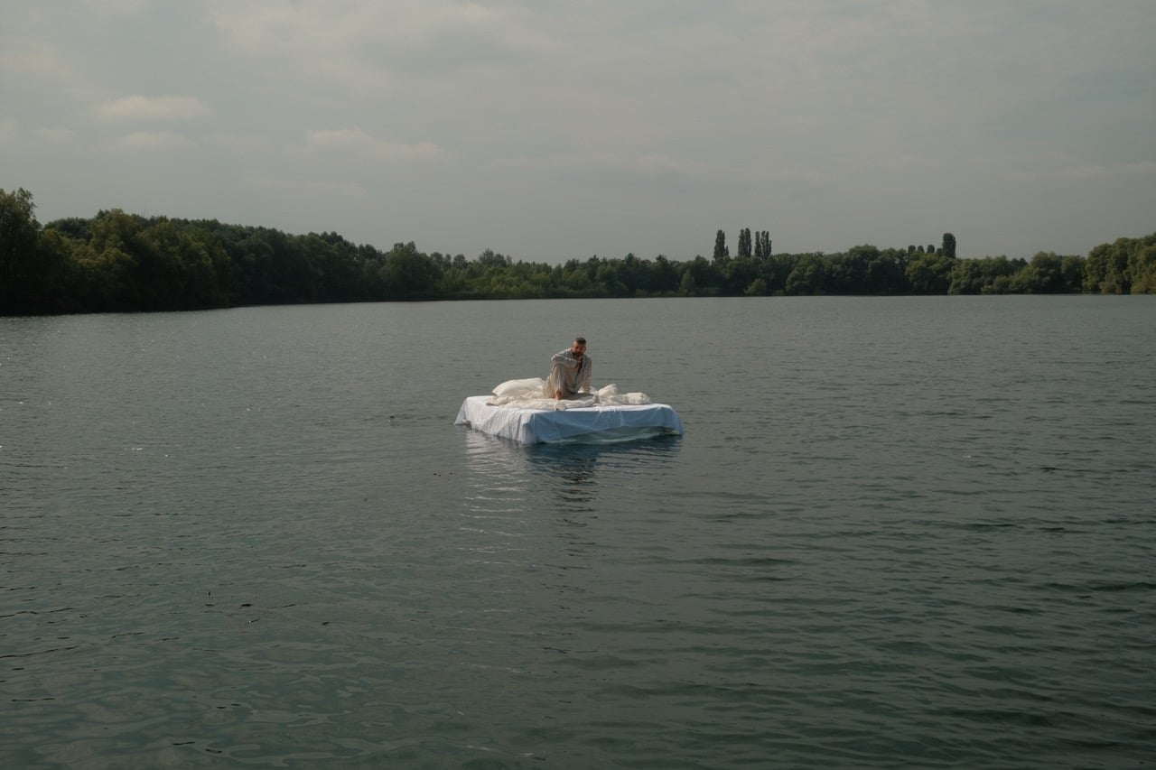 Sido sitzt für sein Musikvideo zu WOKE auf einem Bett mitten im See